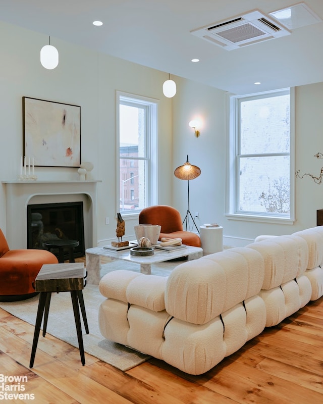 living area with a glass covered fireplace, light wood-style flooring, and visible vents