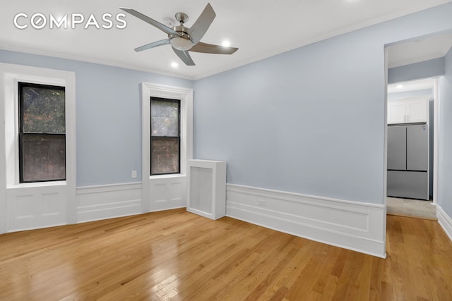 empty room with light wood-style floors, recessed lighting, ceiling fan, a wainscoted wall, and crown molding