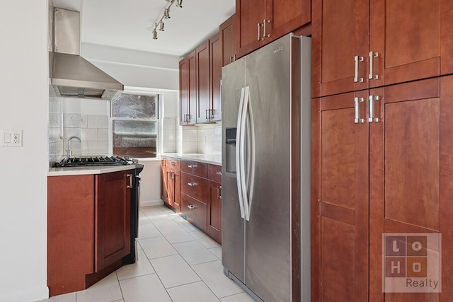 kitchen featuring wall chimney range hood, stainless steel fridge with ice dispenser, light countertops, decorative backsplash, and light tile patterned floors