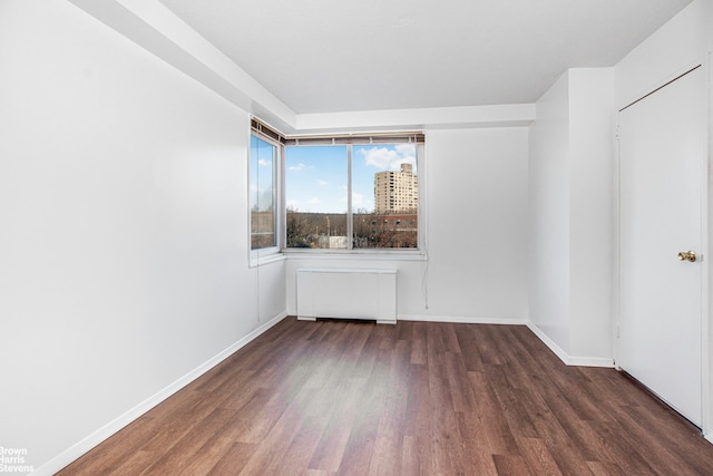 empty room featuring baseboards, radiator, and wood finished floors