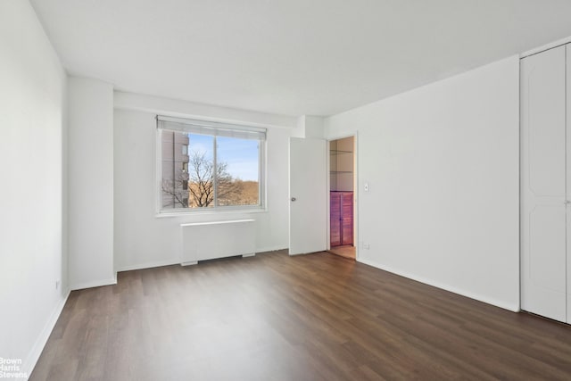 spare room featuring baseboards, radiator, and wood finished floors