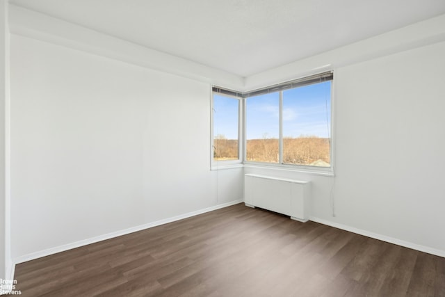 unfurnished room featuring baseboards, dark wood finished floors, and radiator heating unit