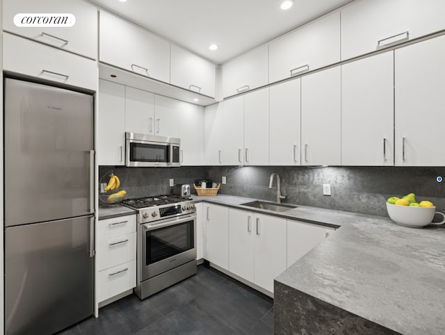 kitchen featuring appliances with stainless steel finishes, a sink, white cabinetry, tasteful backsplash, and dark tile patterned flooring