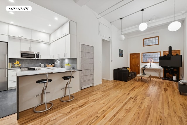 kitchen featuring appliances with stainless steel finishes, open floor plan, a towering ceiling, a sink, and light wood finished floors