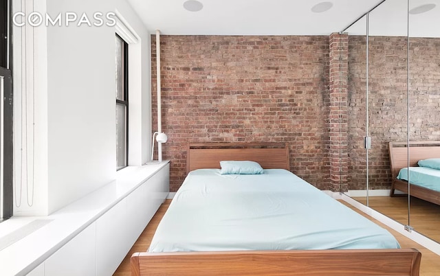 bedroom featuring brick wall and wood finished floors
