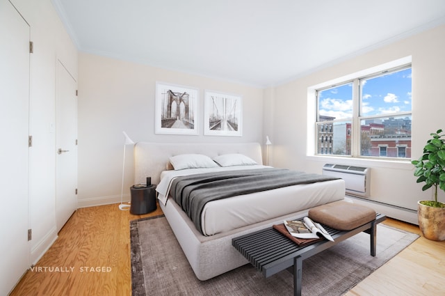 bedroom with baseboard heating, ornamental molding, a wall mounted air conditioner, and light wood-type flooring