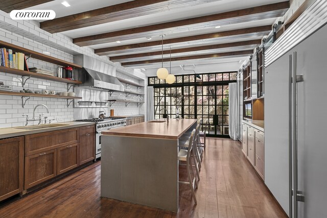 kitchen with wall chimney exhaust hood, open shelves, a sink, premium appliances, and backsplash