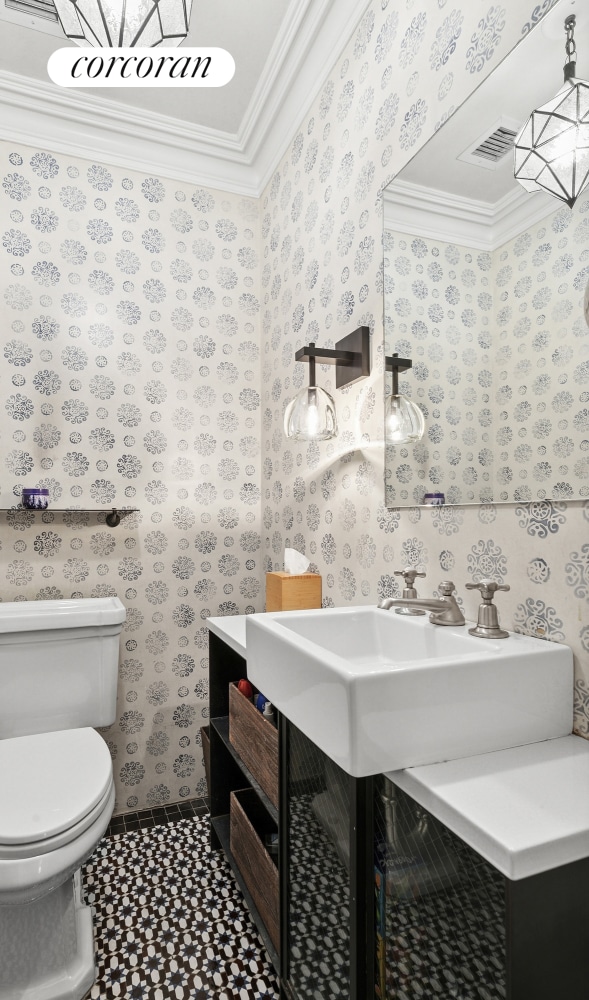 half bath featuring tile patterned floors, wallpapered walls, toilet, ornamental molding, and visible vents