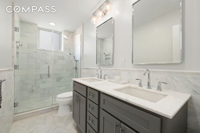 420 E 58th St Unit 14B, New York City, NY 10022 - bathroom featuring tile walls, a stall shower, toilet, double vanity, and wainscoting
