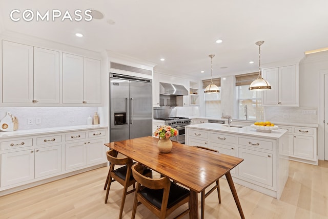 9 W 84th St, New York City, NY 10024 - kitchen featuring high end appliances, wall chimney range hood, light countertops, decorative backsplash, and white cabinetry