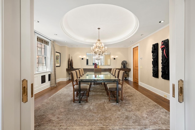 dining area with ornamental molding, a tray ceiling, a chandelier, and wood finished floors