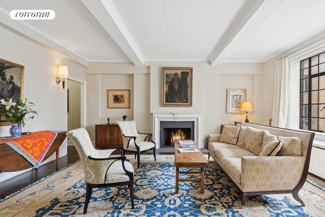 living room featuring beam ceiling, wood finished floors, a fireplace with flush hearth, and ornamental molding