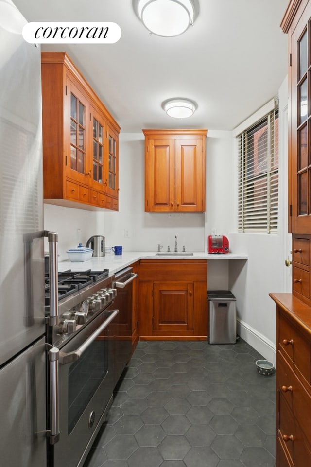kitchen featuring appliances with stainless steel finishes, brown cabinets, glass insert cabinets, light countertops, and a sink