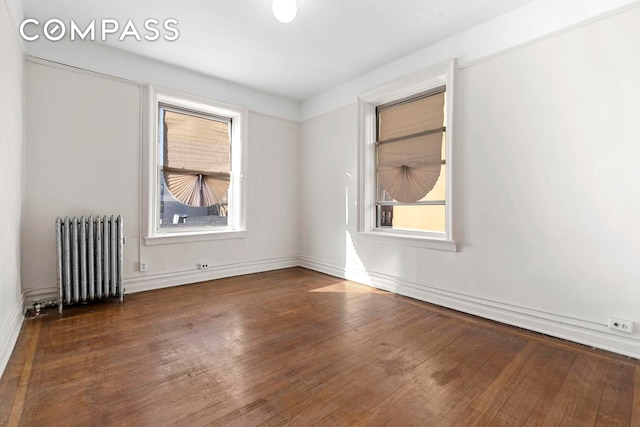 unfurnished room featuring hardwood / wood-style floors, baseboards, radiator, and a wealth of natural light