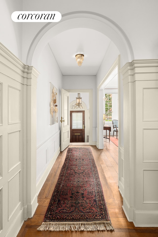 foyer with arched walkways, light wood finished floors, and a decorative wall