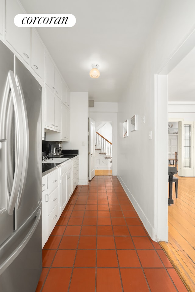 kitchen featuring dark tile patterned flooring, white cabinets, stainless steel fridge, and baseboards