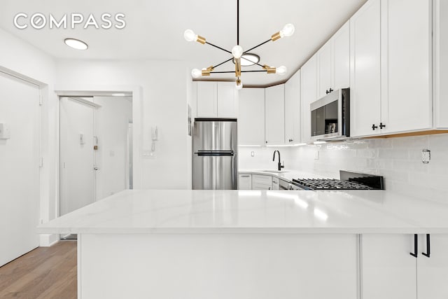 kitchen featuring stainless steel appliances, a sink, tasteful backsplash, a peninsula, and light wood finished floors