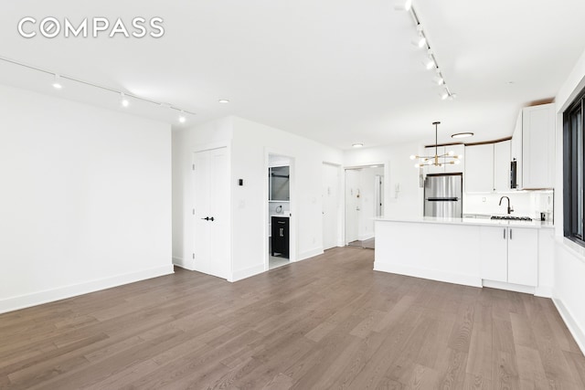 unfurnished living room featuring rail lighting, a chandelier, light wood finished floors, and baseboards