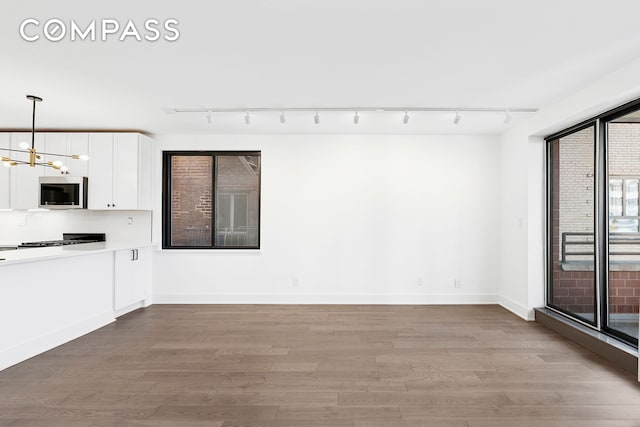 unfurnished living room with track lighting, a chandelier, wood finished floors, and baseboards