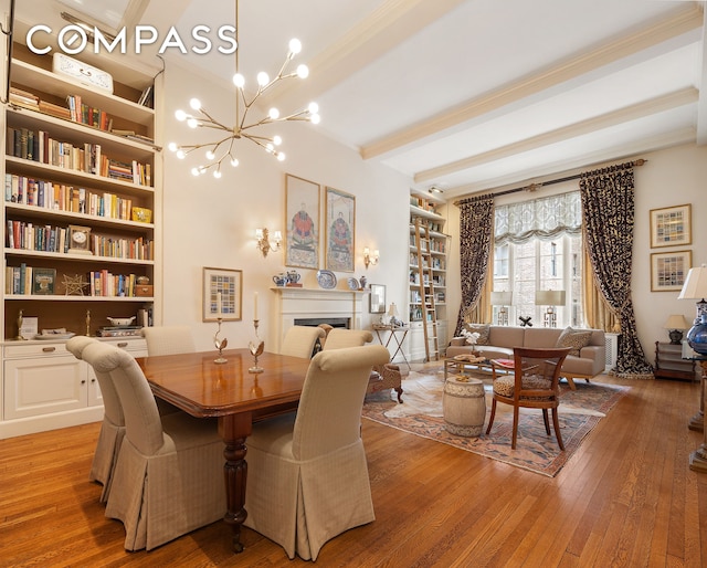 dining area with ornamental molding, light wood-type flooring, a chandelier, beam ceiling, and a fireplace