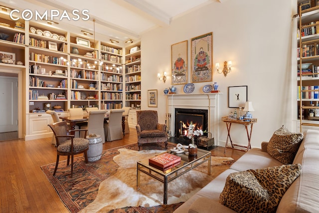 sitting room with hardwood / wood-style flooring, beam ceiling, ornamental molding, a warm lit fireplace, and built in features