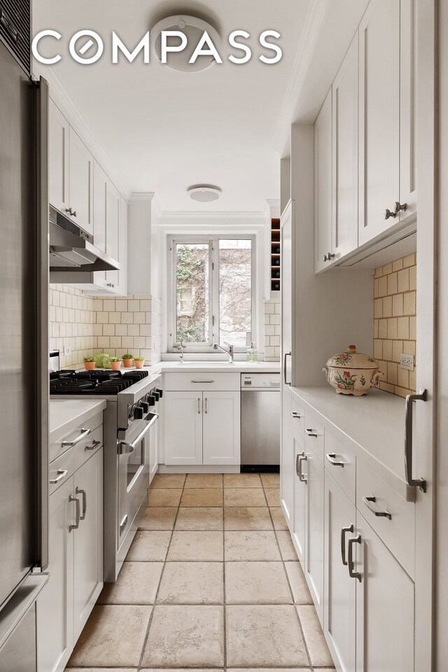 kitchen with appliances with stainless steel finishes, under cabinet range hood, light countertops, decorative backsplash, and ornamental molding