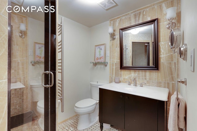 full bathroom with a shower stall, visible vents, toilet, vanity, and tile walls