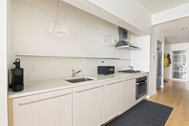 kitchen with wall chimney range hood, a sink, light wood-style flooring, light countertops, and appliances with stainless steel finishes