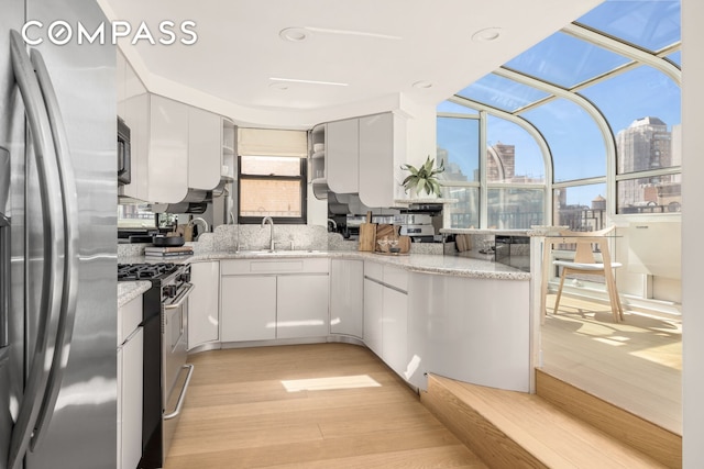 1049 Park Ave Ph, Ph, New York City, NY 10028 - kitchen with stainless steel appliances, a sink, light wood-style floors, a view of skyline, and white cabinetry