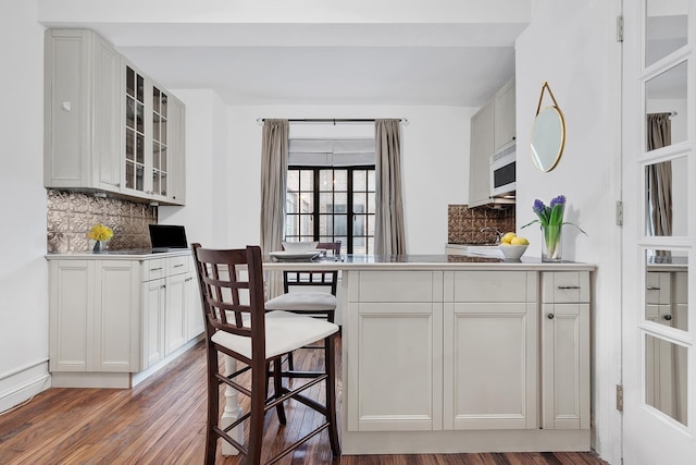 25 Tudor City Pl Unit 1014, New York City, NY 10017 - kitchen featuring decorative backsplash, white microwave, glass insert cabinets, and wood finished floors