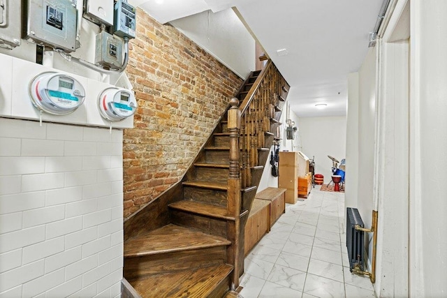 staircase featuring marble finish floor, brick wall, and electric panel