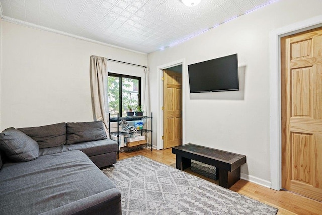 living room featuring crown molding, baseboards, an ornate ceiling, and light wood-style flooring
