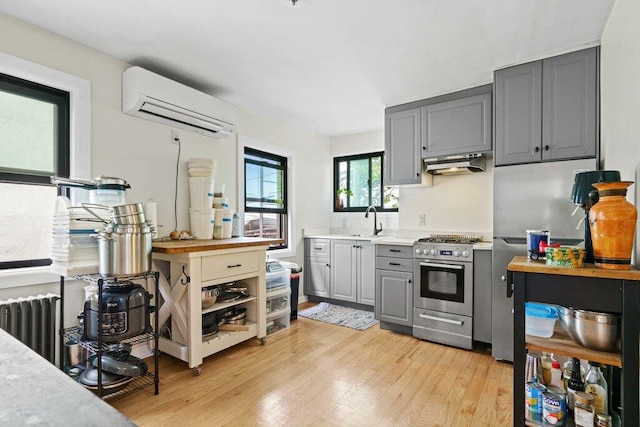 kitchen with a wall mounted air conditioner, stainless steel gas stove, gray cabinetry, a sink, and under cabinet range hood
