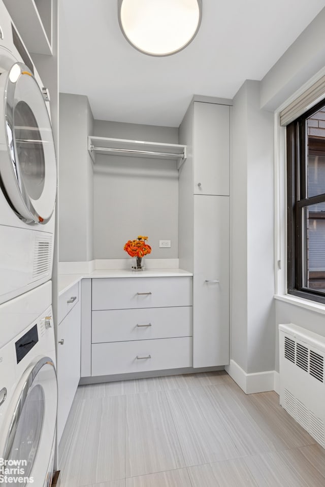 washroom with cabinet space, stacked washer / drying machine, baseboards, and radiator