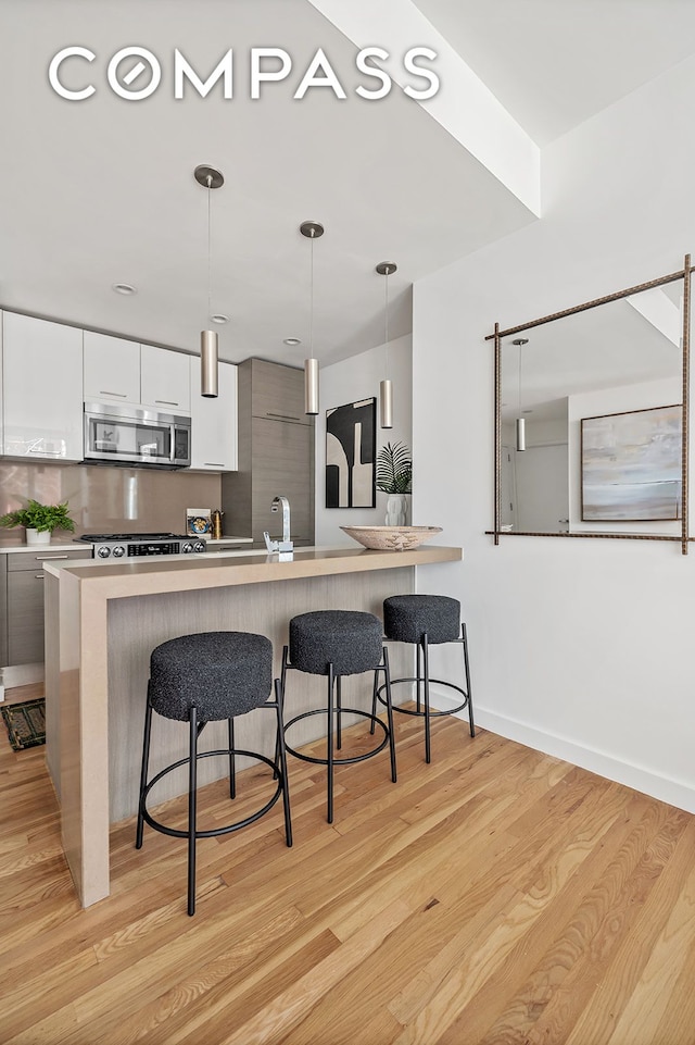 kitchen featuring stainless steel microwave, modern cabinets, a kitchen bar, light wood-style floors, and pendant lighting
