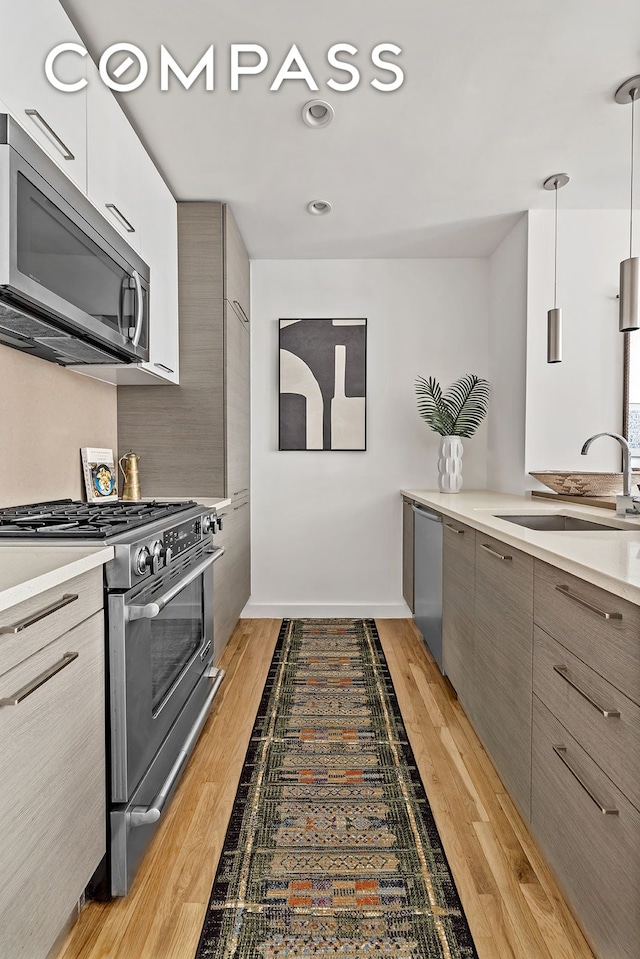 kitchen featuring appliances with stainless steel finishes, modern cabinets, a sink, light countertops, and light wood-type flooring