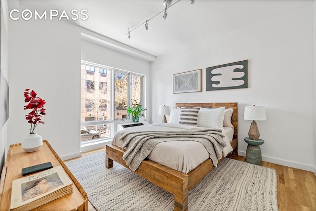 bedroom with rail lighting, wood finished floors, and baseboards