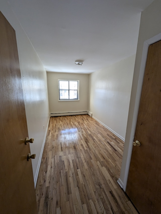 unfurnished room with baseboards, wood finished floors, and a baseboard radiator
