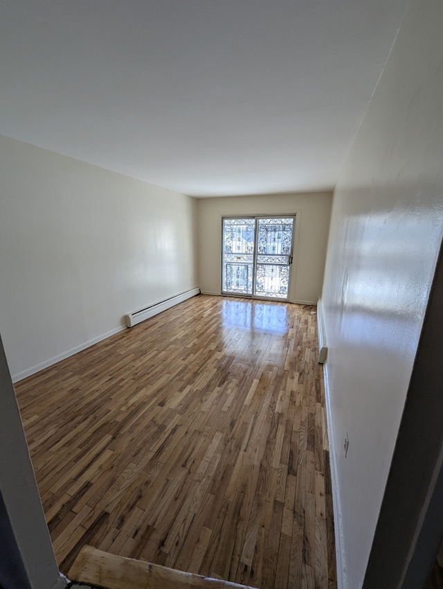 empty room with baseboards, a baseboard heating unit, and wood finished floors