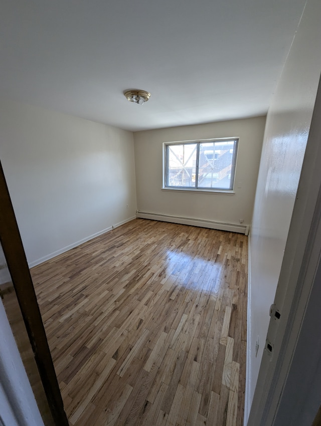 unfurnished room featuring wood finished floors, baseboards, and a baseboard heating unit