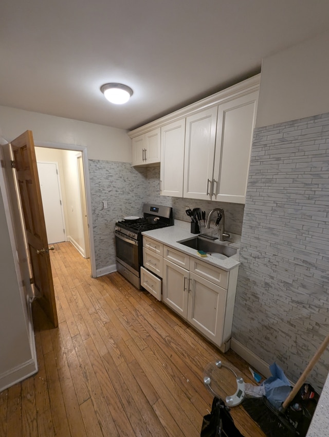 kitchen featuring a sink, light countertops, white cabinets, light wood finished floors, and stainless steel range with gas cooktop
