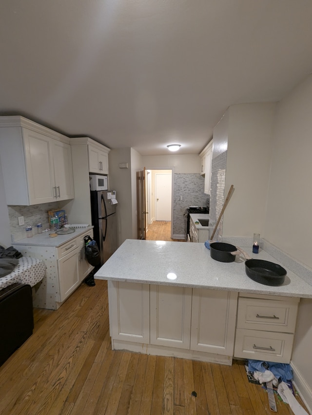 kitchen with light wood-type flooring, freestanding refrigerator, a peninsula, and white cabinets