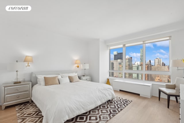 100 United Nations Plz Unit 35E, New York City, NY 10017 - bedroom featuring radiator heating unit, a view of skyline, and light wood-style floors