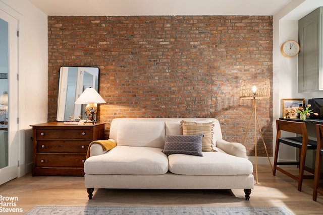 living area with light wood finished floors, brick wall, and baseboards