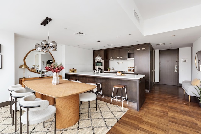 kitchen featuring dark brown cabinets, light countertops, wood finished floors, a breakfast bar area, and a chandelier