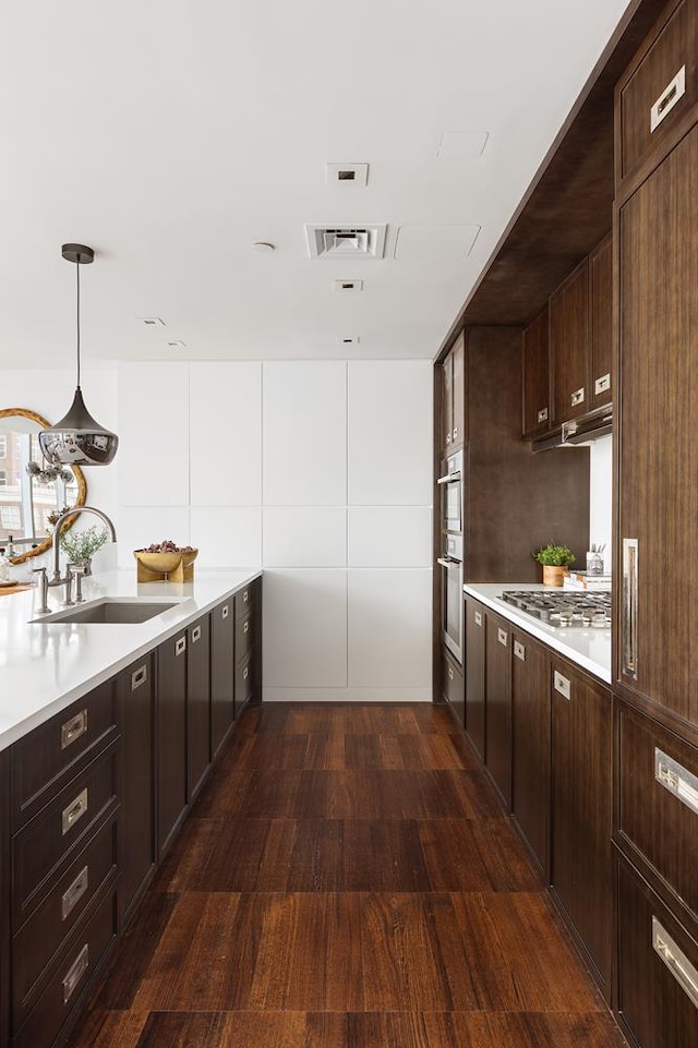 kitchen featuring a sink, dark wood-type flooring, light countertops, dark brown cabinets, and decorative light fixtures