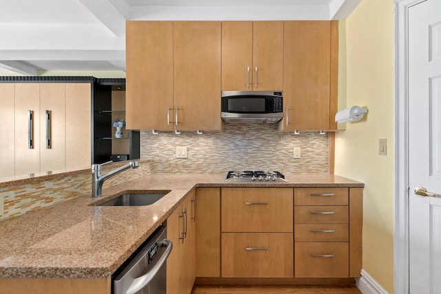 kitchen featuring appliances with stainless steel finishes, a sink, tasteful backsplash, light stone counters, and a peninsula