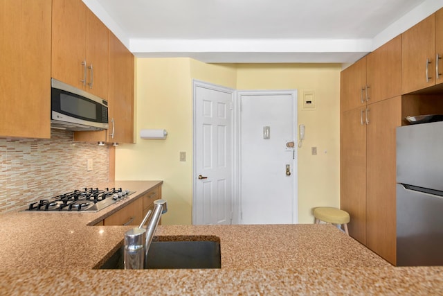 235 W 102nd St Unit 12F, New York City, NY 10025 - kitchen featuring stainless steel appliances, light stone counters, tasteful backsplash, a sink, and brown cabinetry