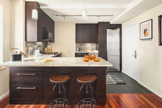 kitchen with dark brown cabinets, black microwave, stainless steel refrigerator, a peninsula, and decorative backsplash
