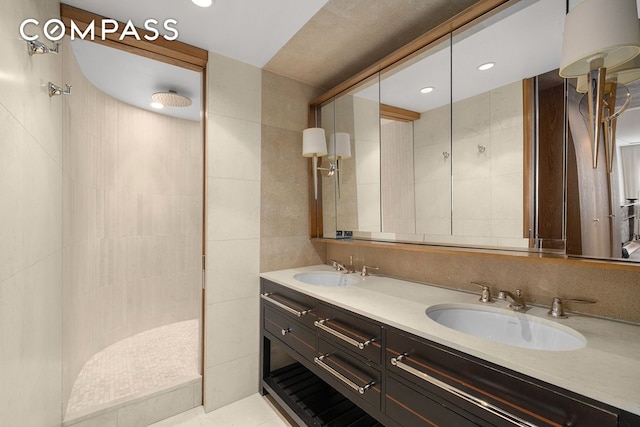 bathroom featuring tile walls, tiled shower, double vanity, and tile patterned flooring